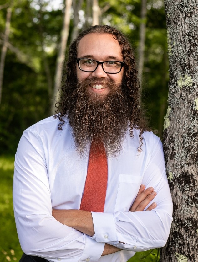 Nathaniel Moore smiling in a forest wearing a white shirt